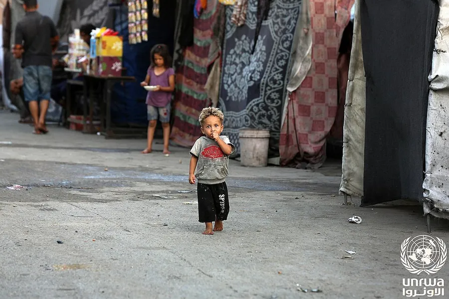 A displaced child in front of a tent at a shelter in Gaza